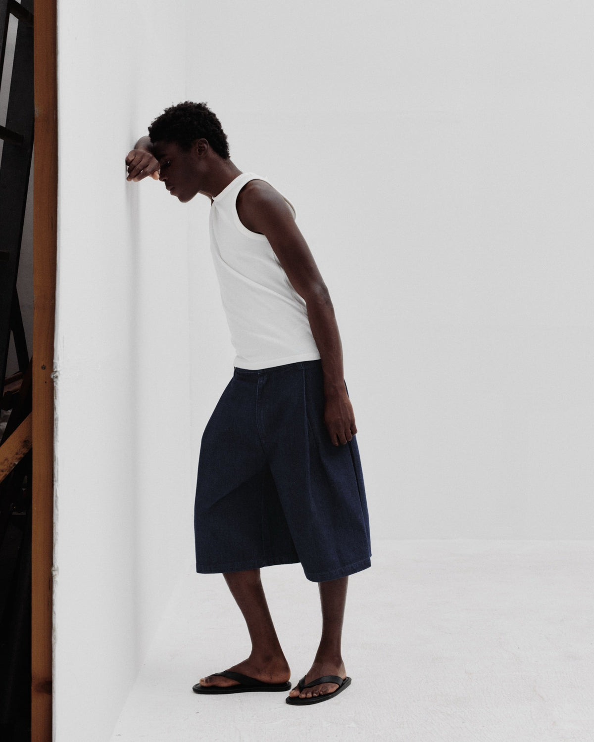 REAMO Denim lookbook – model in navy wide shorts leaning on a white wall