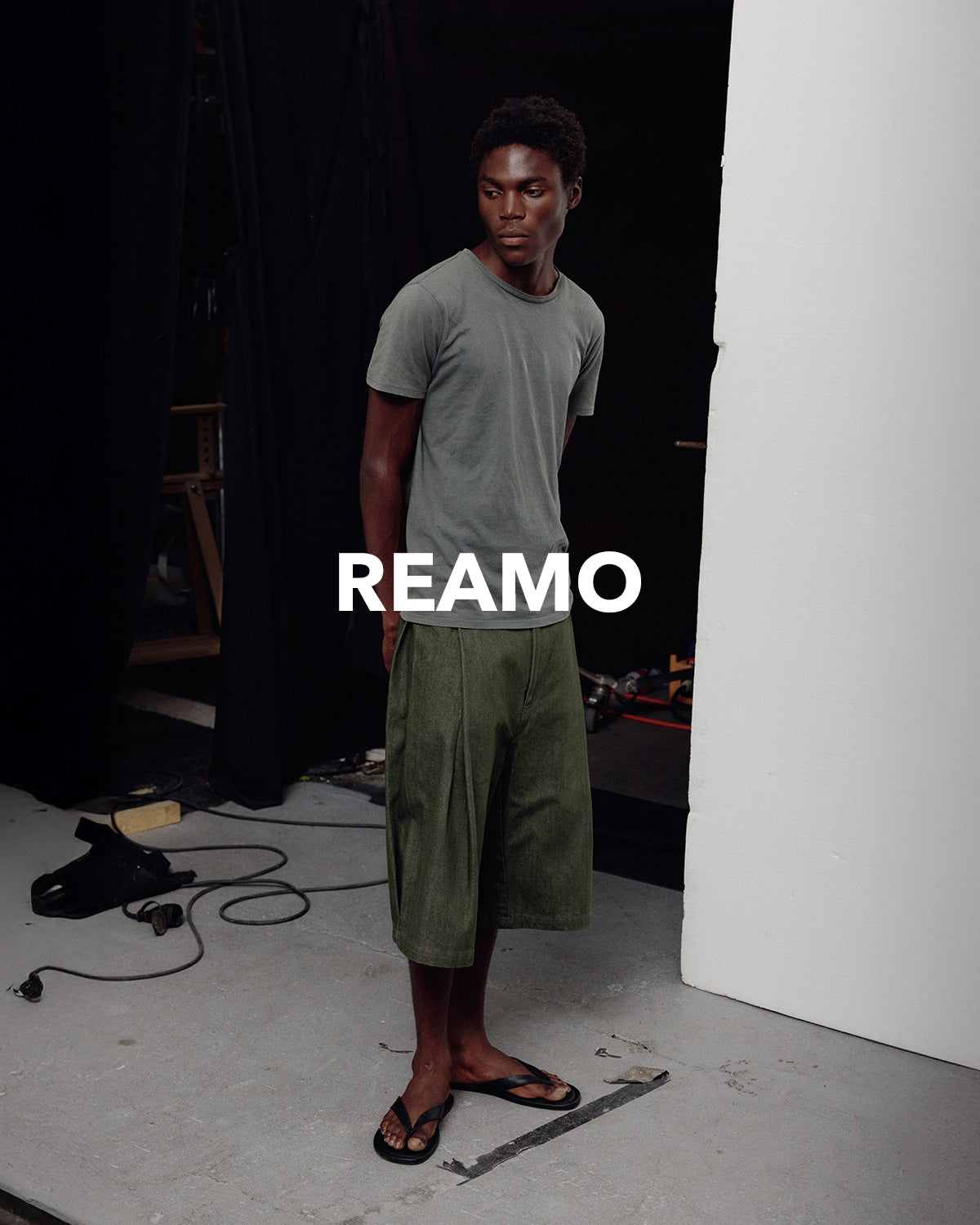 REAMO Denim lookbook – olive wide shorts with a grey T-shirt by the studio wall